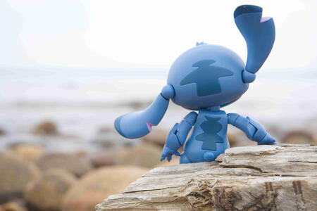Stitch from Lilo and Stitch, sitting on a log and looking out at the water on an overcast day