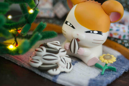 toy photography of hamtaro eating sunflower seeds next to a christmas tree